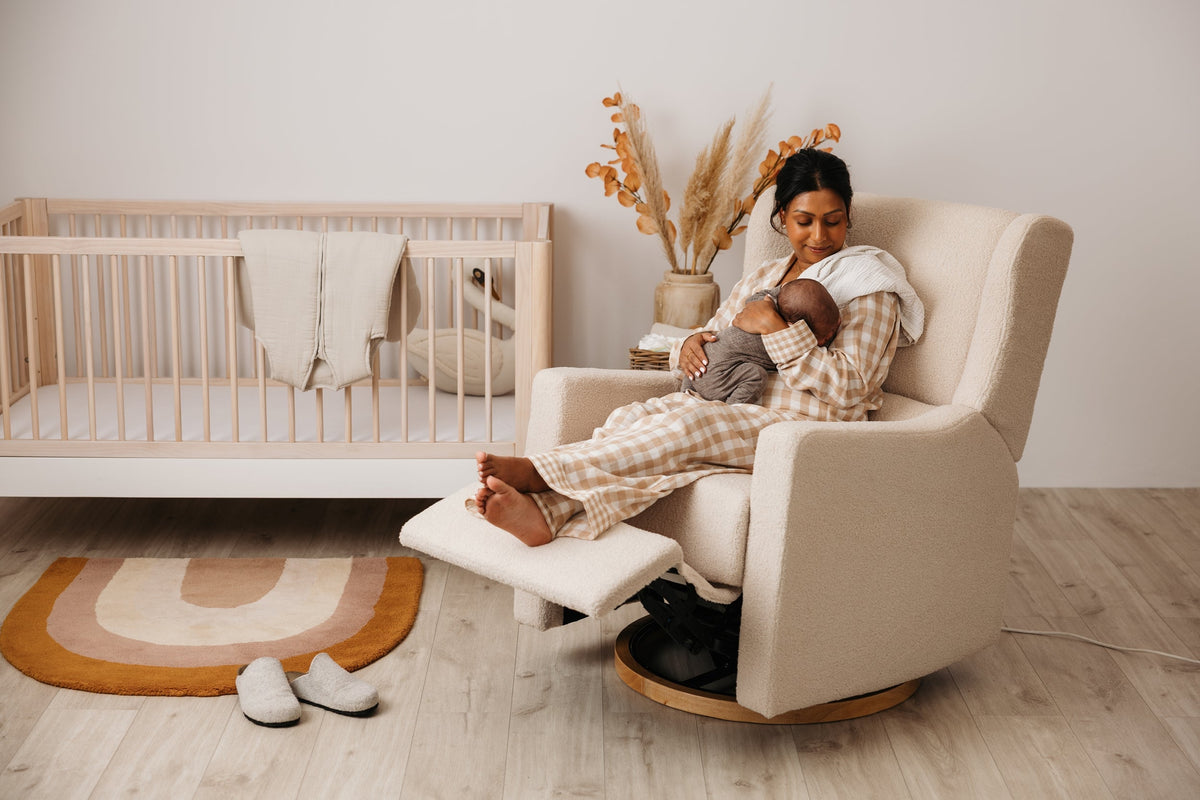 Mother and baby resting in the Gaia Baby Lyra electric recliner in Biscuit Bouclé beside a cot