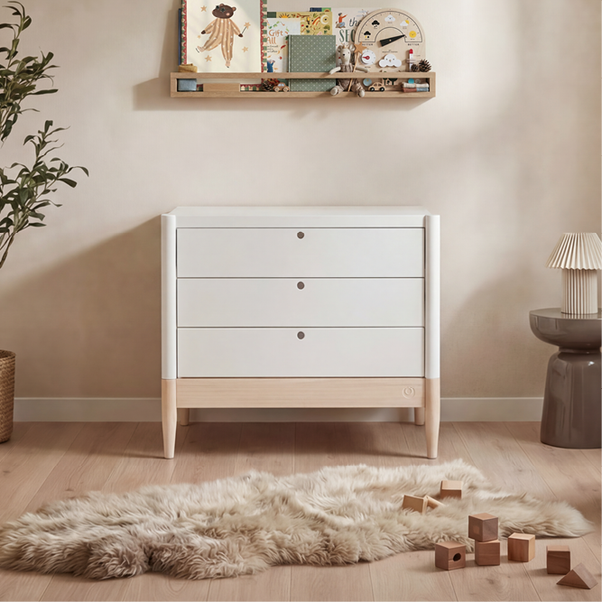 White Gaia Baby Eos dresser with natural wood accents, featuring multiple drawers for organized nursery storage.