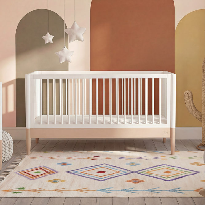 White Gaia Baby EOS cot bed with powder blush accents, featuring a sturdy wooden frame and slatted sides for safe infant sleep.