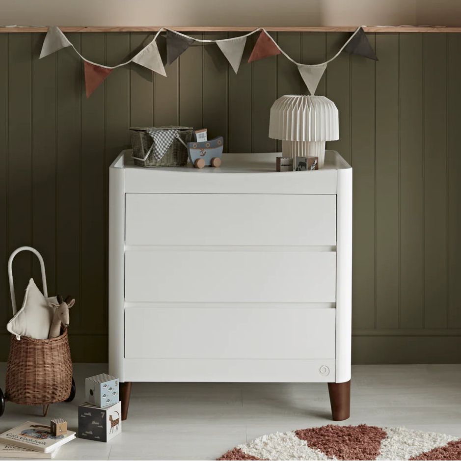White Gaia Baby Serena dresser with walnut legs, featuring sleek design and spacious drawers for nursery storage.