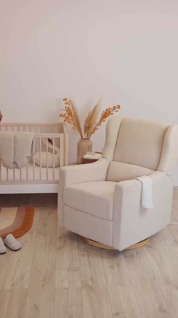 Mother holding her baby in the Gaia Baby Lyra nursing chair in Biscuit Bouclé beside a cot