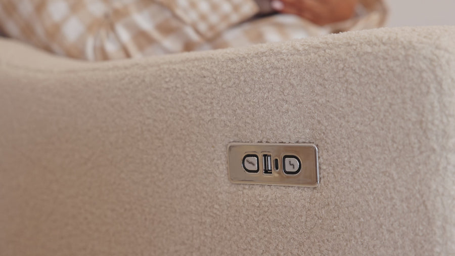 A hand pressing the recline control on the arm of the Lyra nursing chair in Biscuit Bouclé