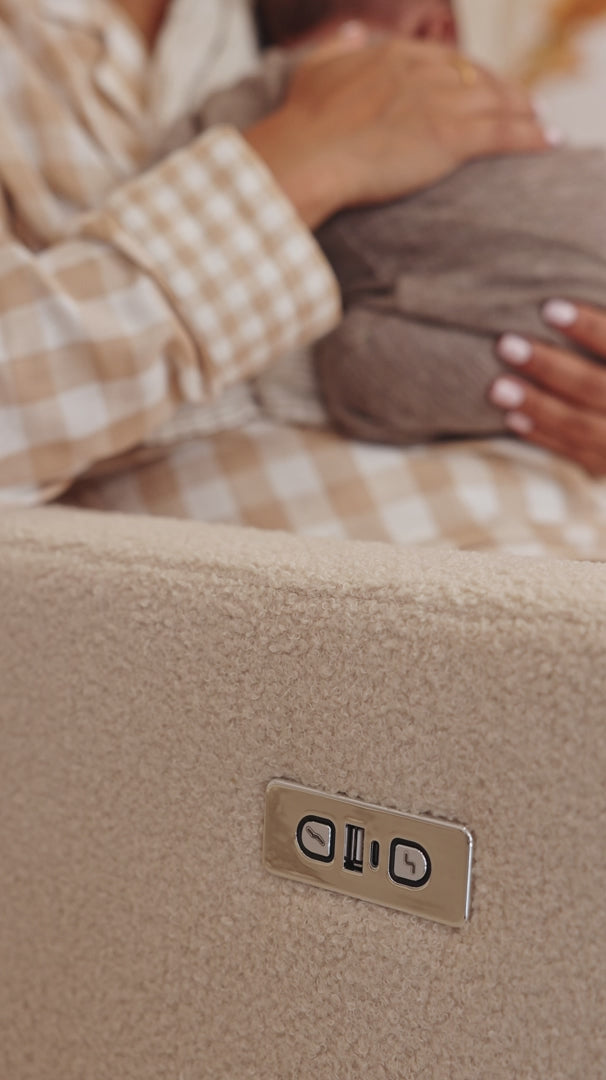 A hand on the recline control of the Lyra nursing chair in Biscuit Bouclé with a baby resting nearby